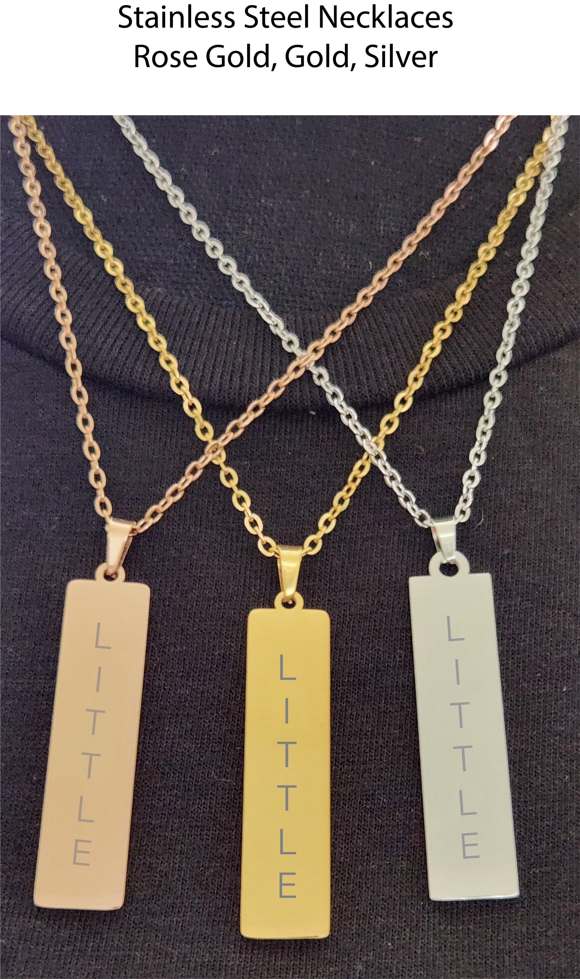 Three necklaces with 'LITTLE' pendants on a dark fabric background